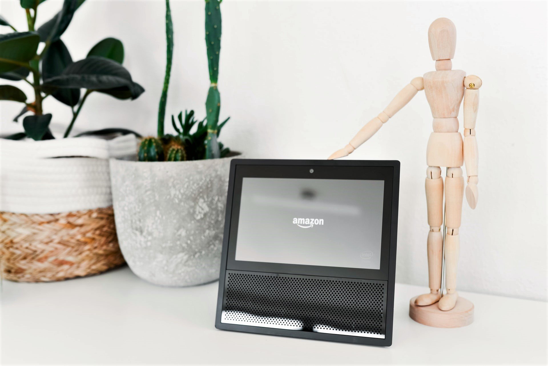 wooden mannequin standing next to an Echo show device on a white table.