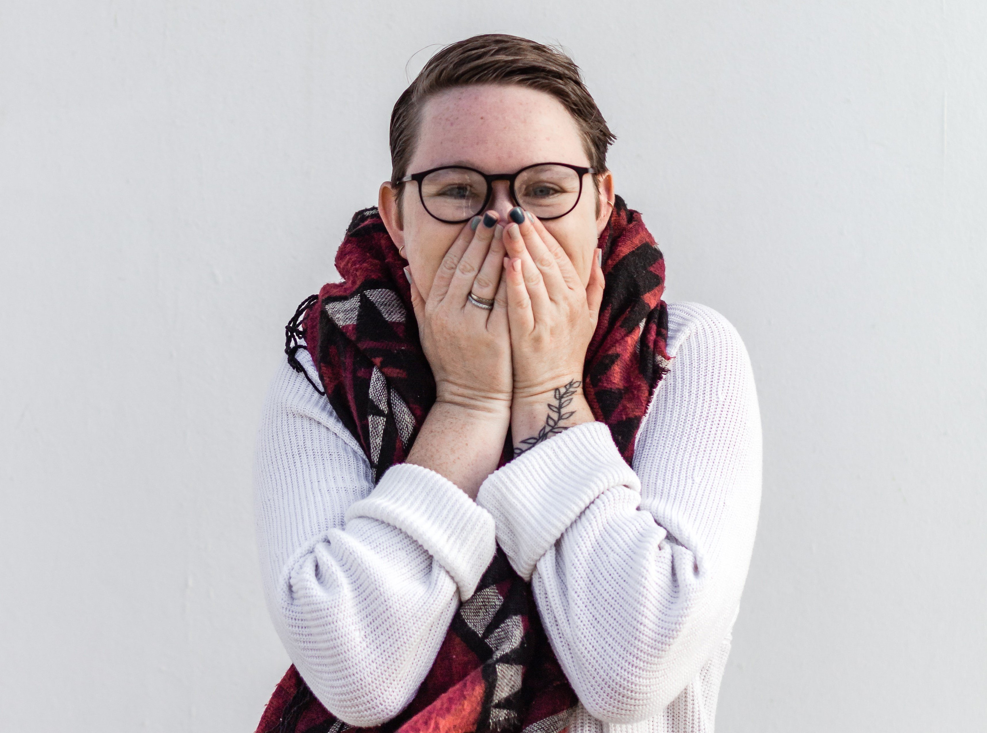 Happy short-haired woman covering her mouth with both hands.